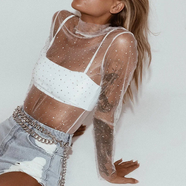 Person wearing a sheer top with white polka dots and denim shorts on a light background